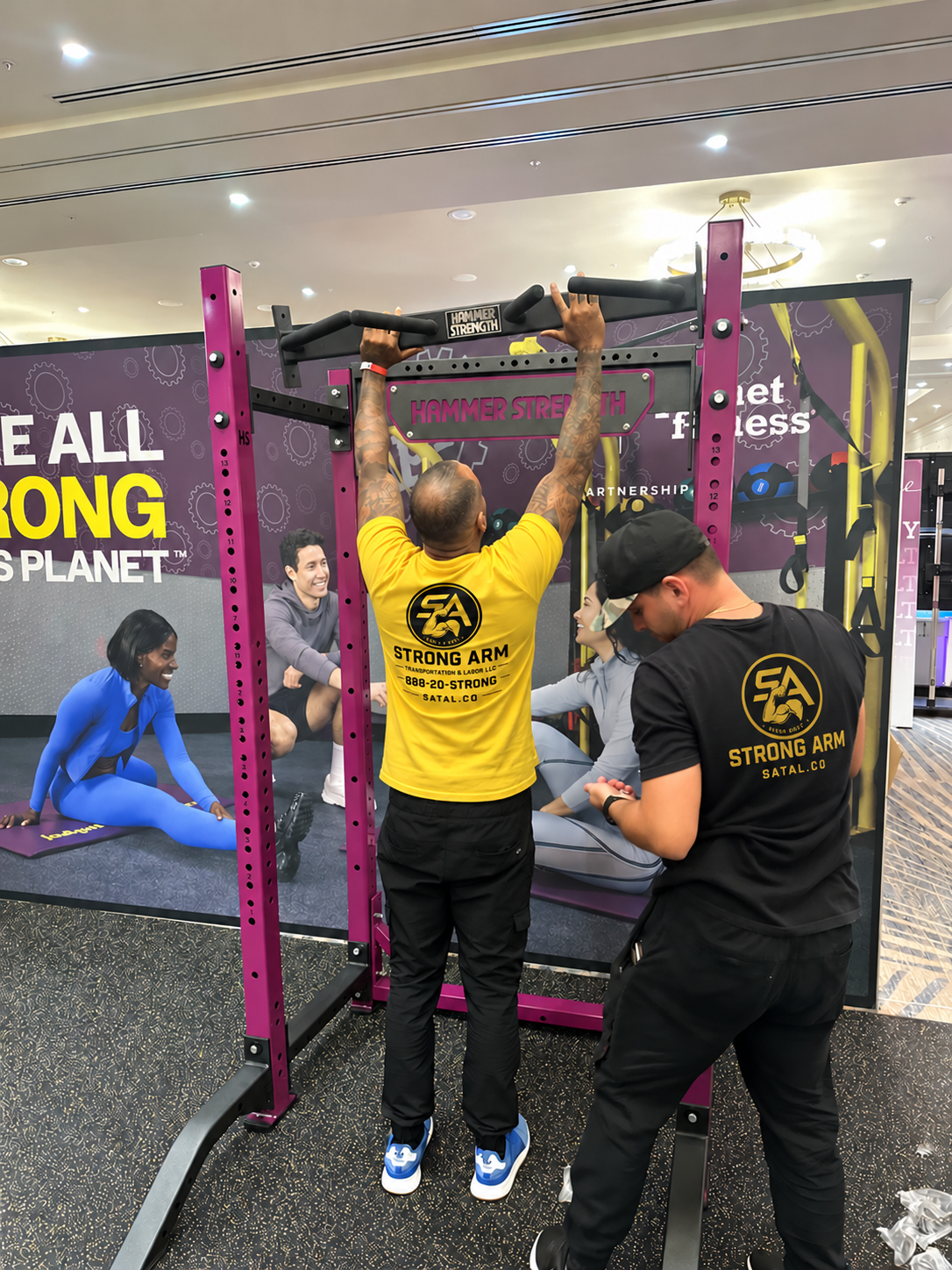 StrongArm crew assembling Hammer Strength rack at Planet Fitness trade show